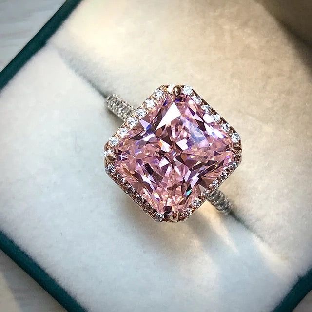 a pink diamond ring sitting on top of a white velvet box with diamonds around it