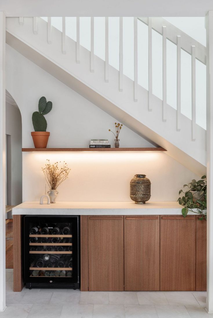 a wine cooler in the middle of a kitchen under a stair case with potted plants on top