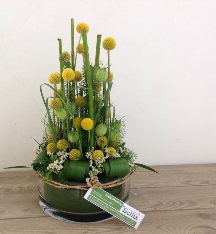 an arrangement of flowers in a green bowl on a wooden table with a price tag