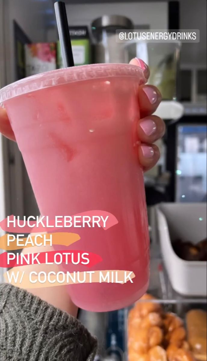 a person holding up a pink drink in front of doughnuts