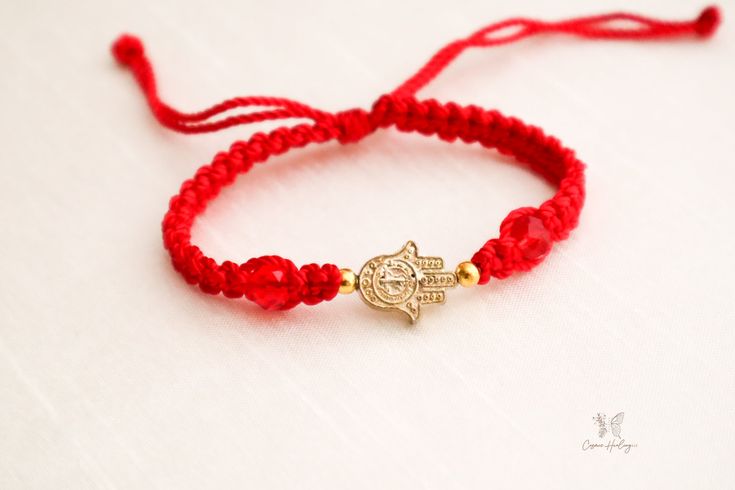 The Fatima Hand Charm Bracelet is a perfect gift for the loved one in your life. It's made from a high quality woven thread that can stretch to fit most any wrist size, showcasing a gold Hamsa hand against a crimson backdrop. Hamsa, meaning "five" in Arabic, is a symbol of protection, luck, and sometimes specifically the "hand of God." Wear the Hamsa hand to keep you in good health and ward off the evil eye. Use it to give as a great gift for someone you care about to let them know you're always Gold Hand-strung Friendship Bracelets As Gift, Gold Braided Bracelets With Adjustable Length As Gift, Red Hand-strung Friendship Stretch Bracelet, Adjustable Braided Bracelets, Hand-strung, Gift, Gold Hand Wrapped Friendship Bracelets As Gift, Red Macrame Beaded Bracelets For Friendship, Gold Beaded Braided Bracelet As Gift, Bohemian Gold Braided Bracelets Gift, Gold Bohemian Braided Bracelets Gift