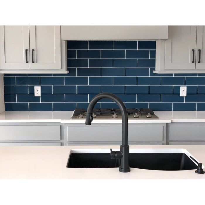 a kitchen sink with a black faucet in front of blue tiled backsplash