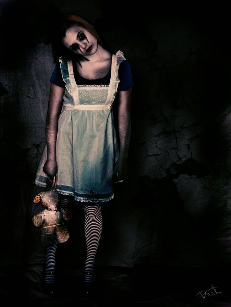 a creepy woman holding a teddy bear in her hand and looking down at the ground