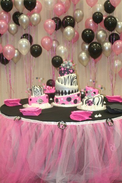 a table topped with two cakes covered in pink and black frosted cake next to balloons