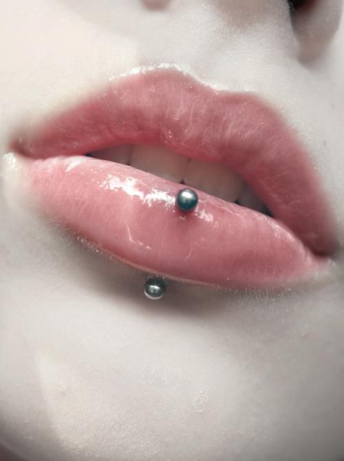 a woman's pink lip with a piercing on the tip and green balls in her mouth