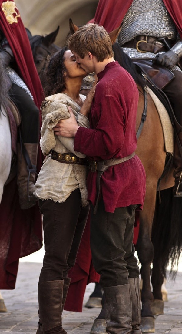 a man and woman kissing in front of some horses on the street with red capes