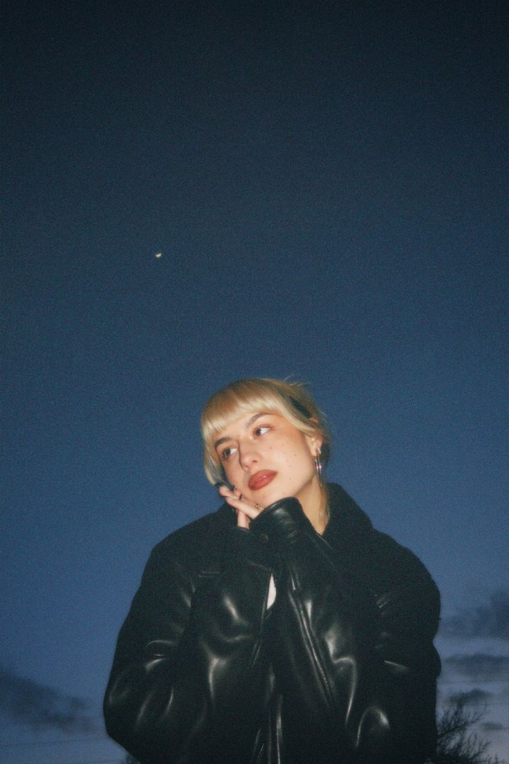 a woman wearing a black leather jacket standing in front of a dark sky at night