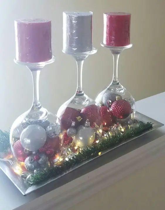 three wine goblets with candles and ornaments in them on a glass platter