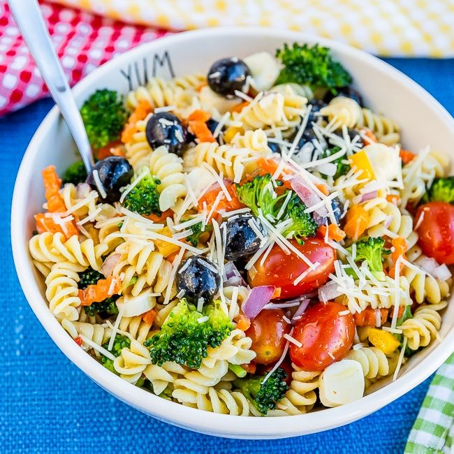 a white bowl filled with pasta salad on top of a blue and white checkered table cloth