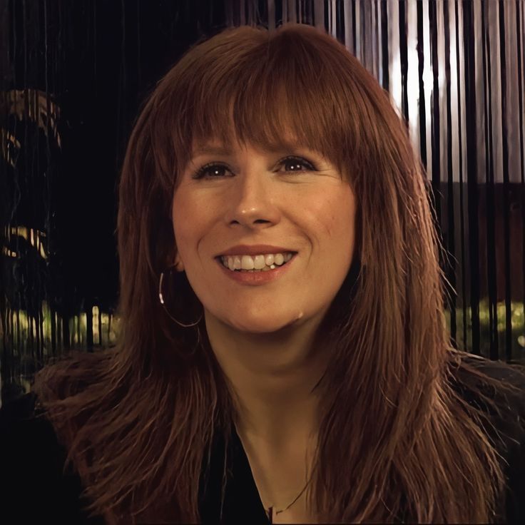 a woman with long brown hair and bangs smiling at the camera while wearing a black shirt