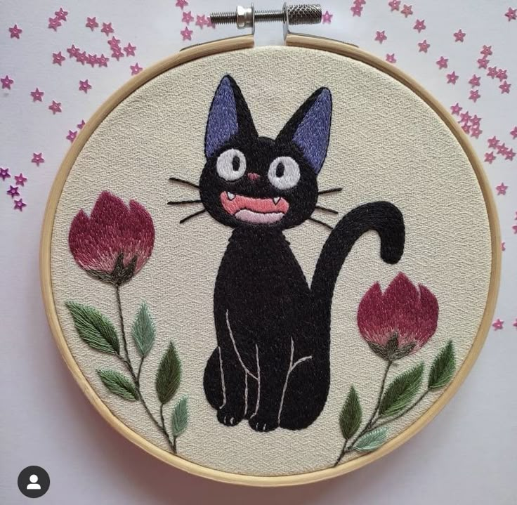 a black cat is sitting in front of some pink flowers on a white wall hanging