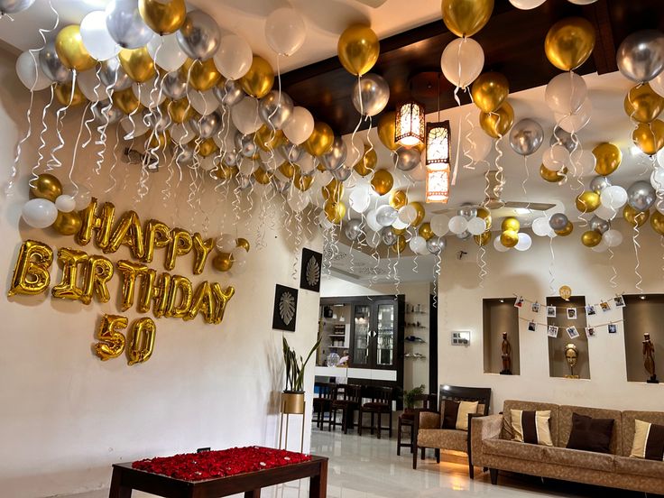 balloons and streamers are hanging from the ceiling in this birthday party room with gold, white and silver decorations