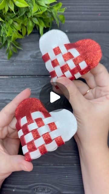 two hands are holding red and white slippers on top of a wooden table with greenery in the background