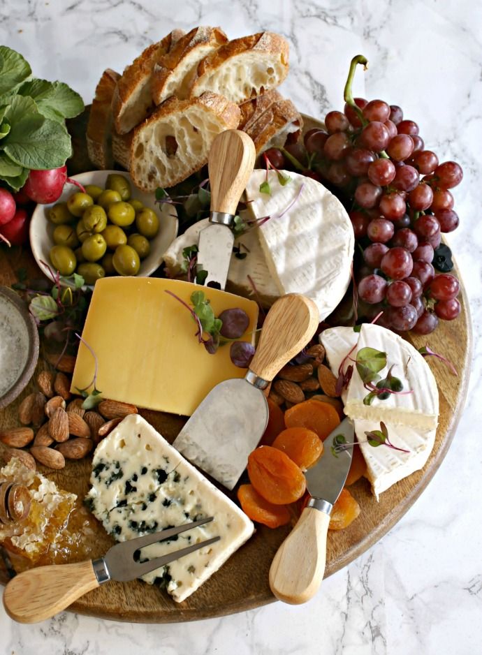 an assortment of cheeses, crackers and nuts on a platter with grapes