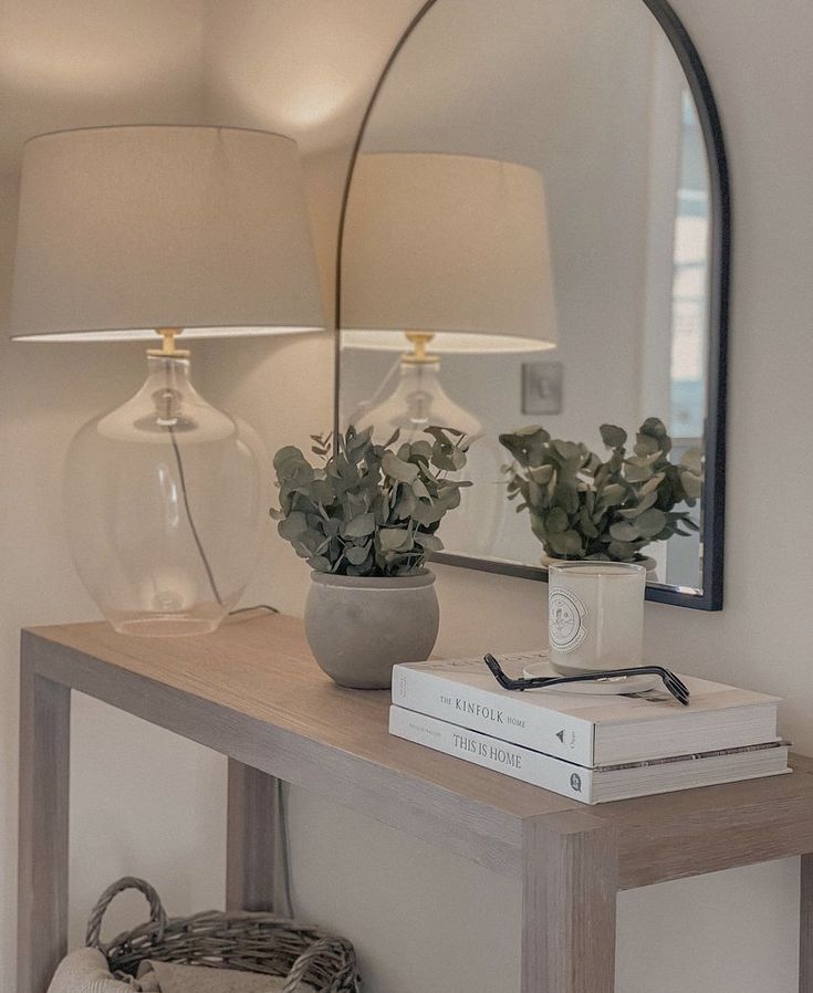 a table with a mirror, lamp and books on it next to a basket filled with plants