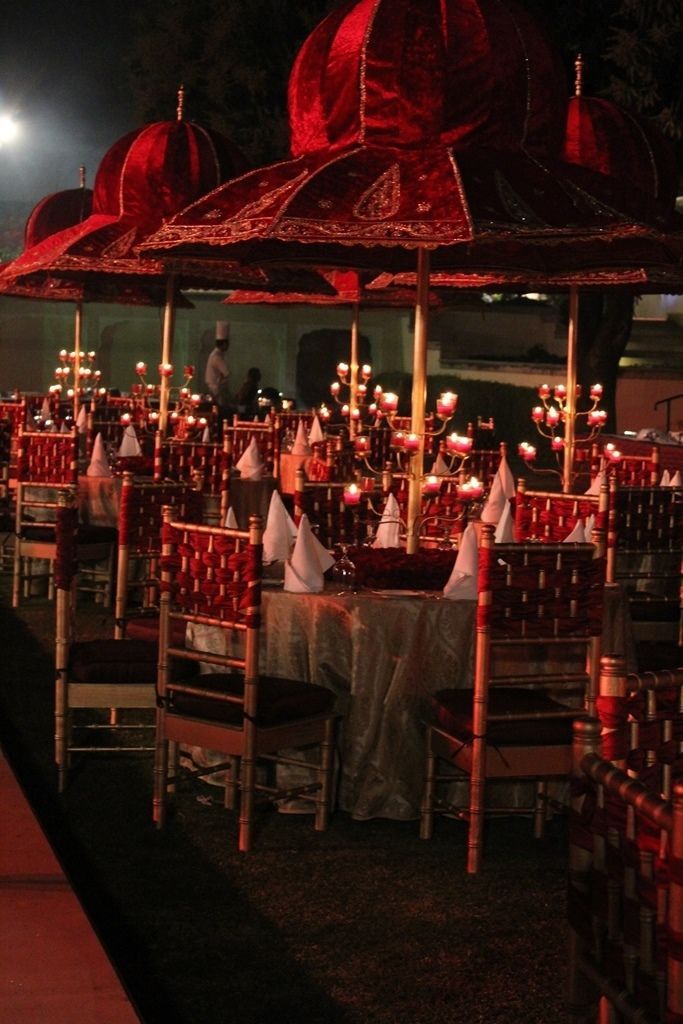 an outdoor dining area with tables and chairs covered in red umbrellas at night time