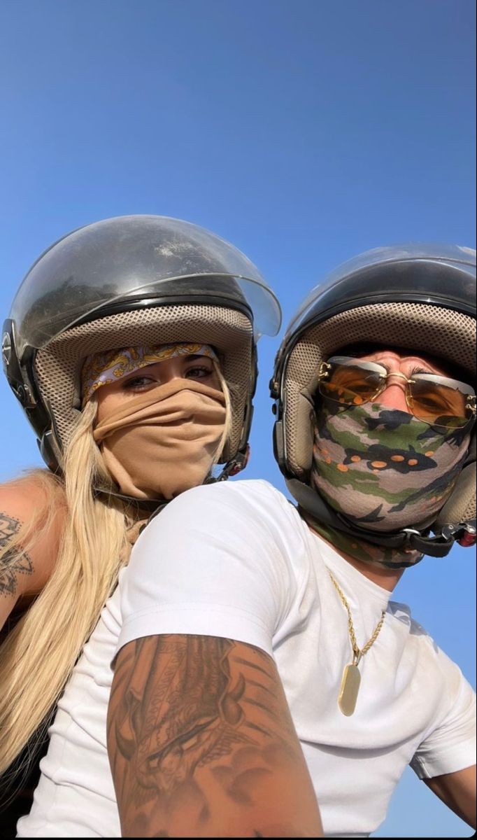 two people wearing helmets and tattoos on their faces are posing for the camera with each other