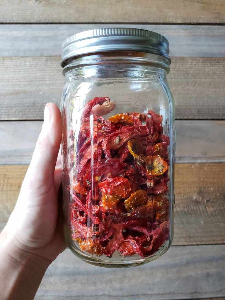 a person holding up a jar filled with dried fruit and veggies on top of a wooden table