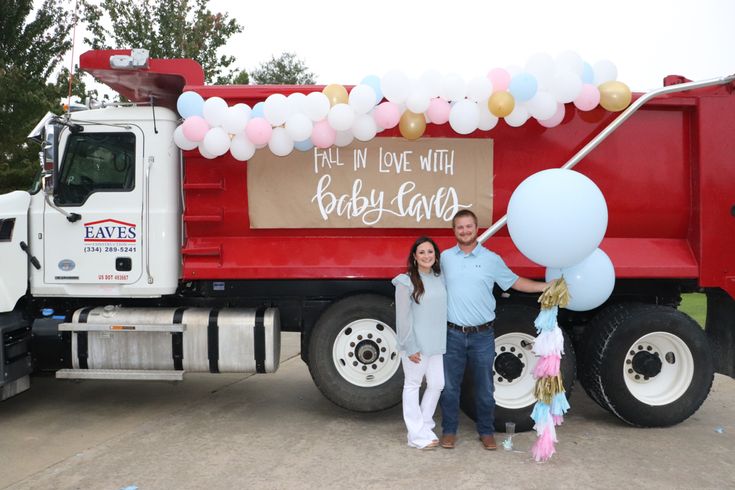 a man and woman standing in front of a red dump truck with balloons on it