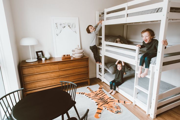 two children climbing on bunk beds in a room with white walls and wood flooring