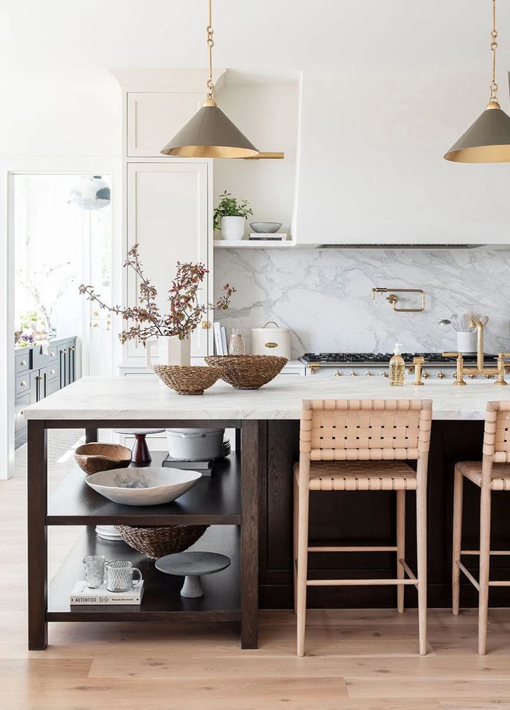 a kitchen with marble counter tops and two pendant lights hanging over the island in front of it