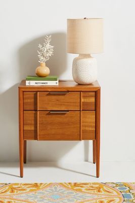 a wooden table with a lamp on top of it next to a rug and a white wall