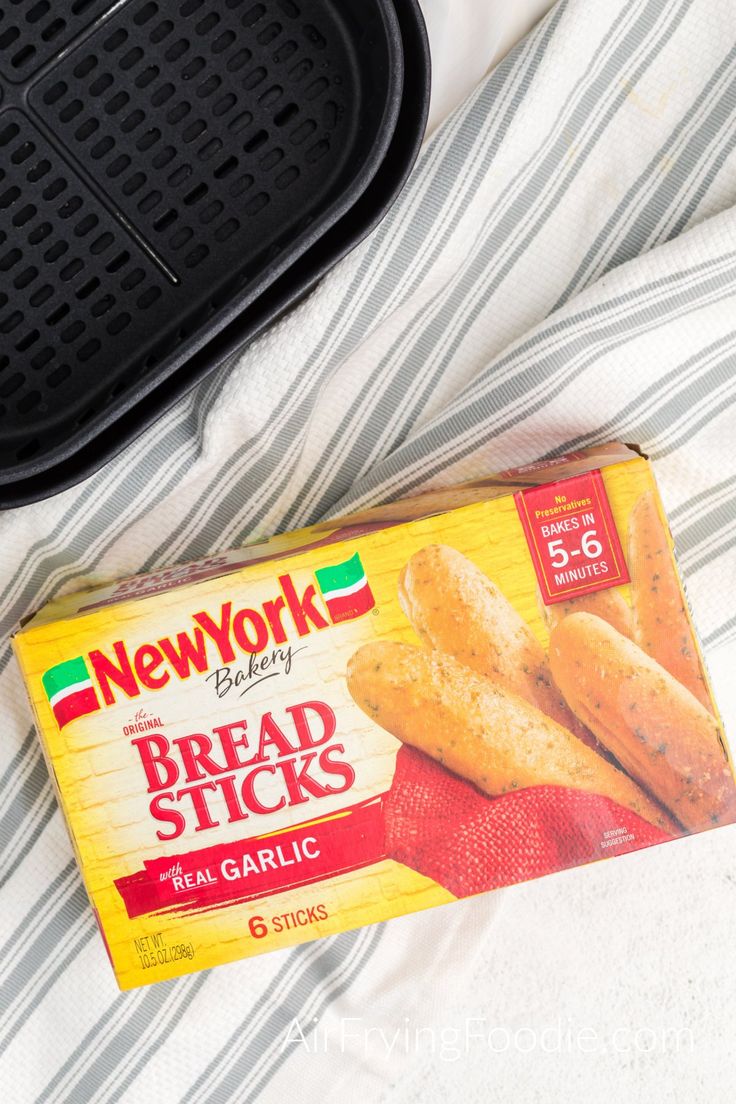 a box of bread sticks sitting on top of a bed next to an air fryer