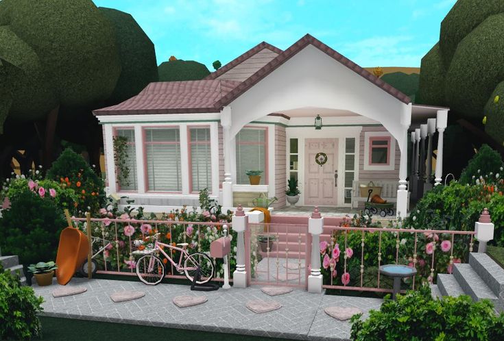 a small pink house with a bicycle parked in the front yard and flowers around it