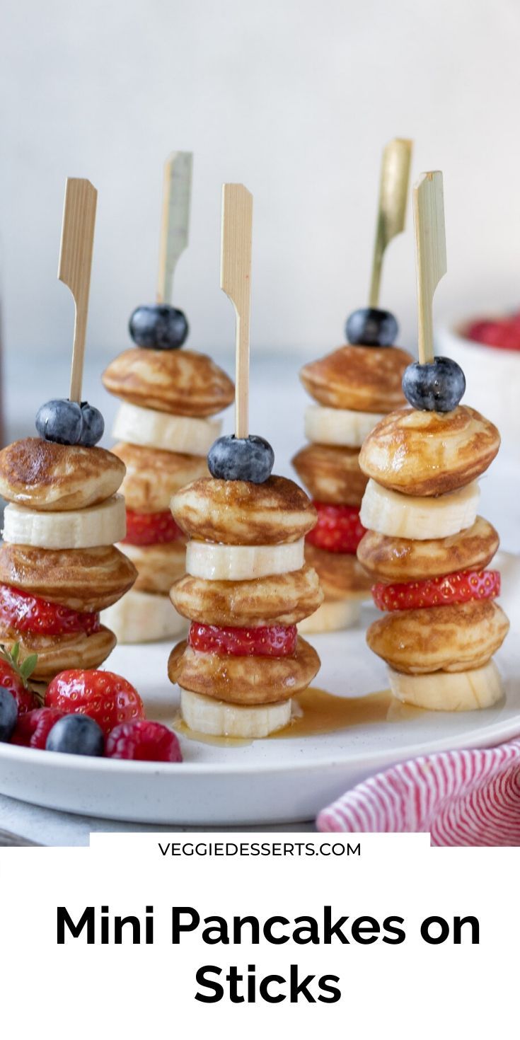 pancakes on sticks with berries and blueberries are arranged on a white platter for an appetizer