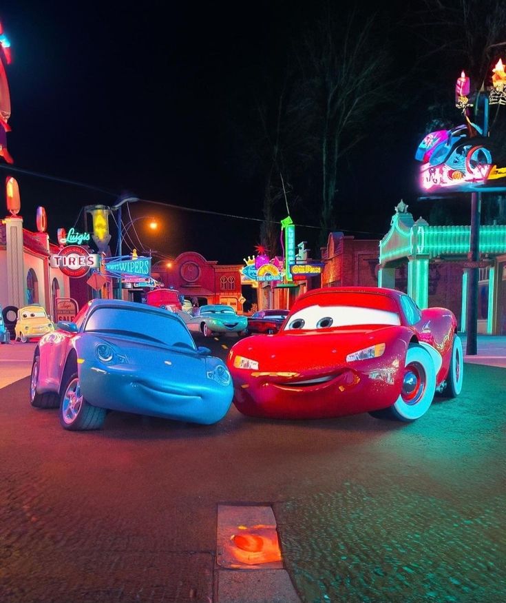 cars lined up on the street at night in front of neon signs and carnival rides