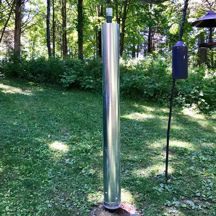 a metal pole in the middle of a grassy area next to a bird feeder and trees