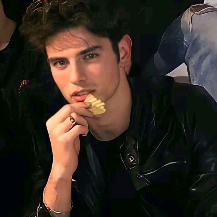 a young man is eating something with his hand and looking at the camera while wearing a black leather jacket