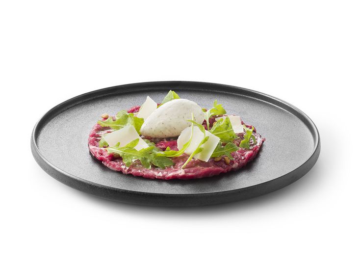 a black plate topped with meat and lettuce on top of a white table