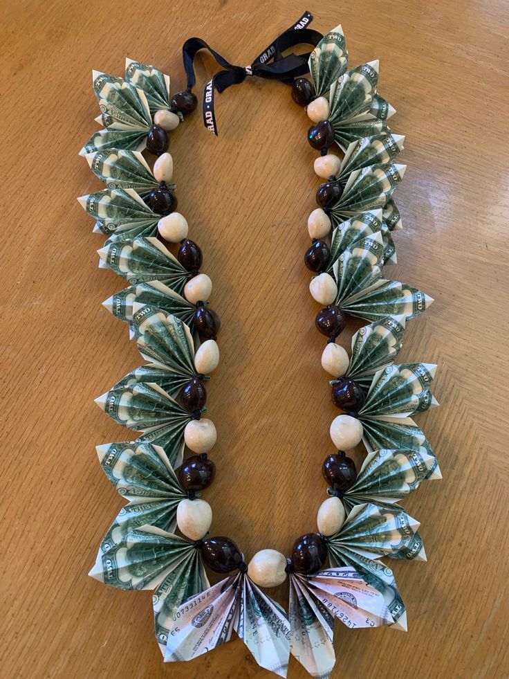 a necklace made out of green and white beads on a wooden table with black ribbon