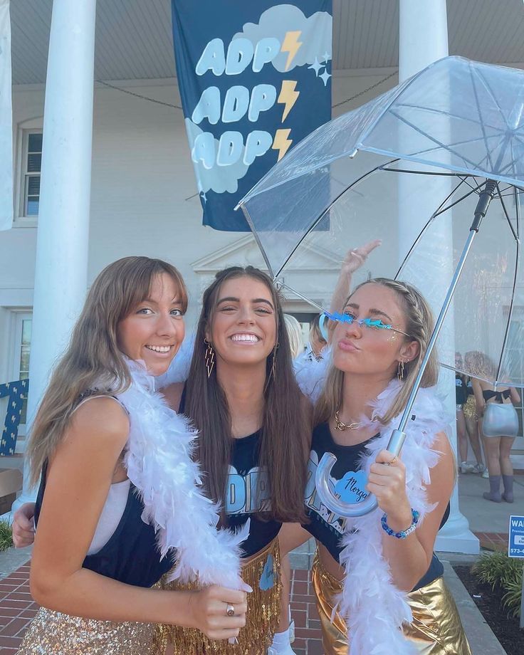 three girls are dressed up and posing for the camera with an umbrella in front of a building