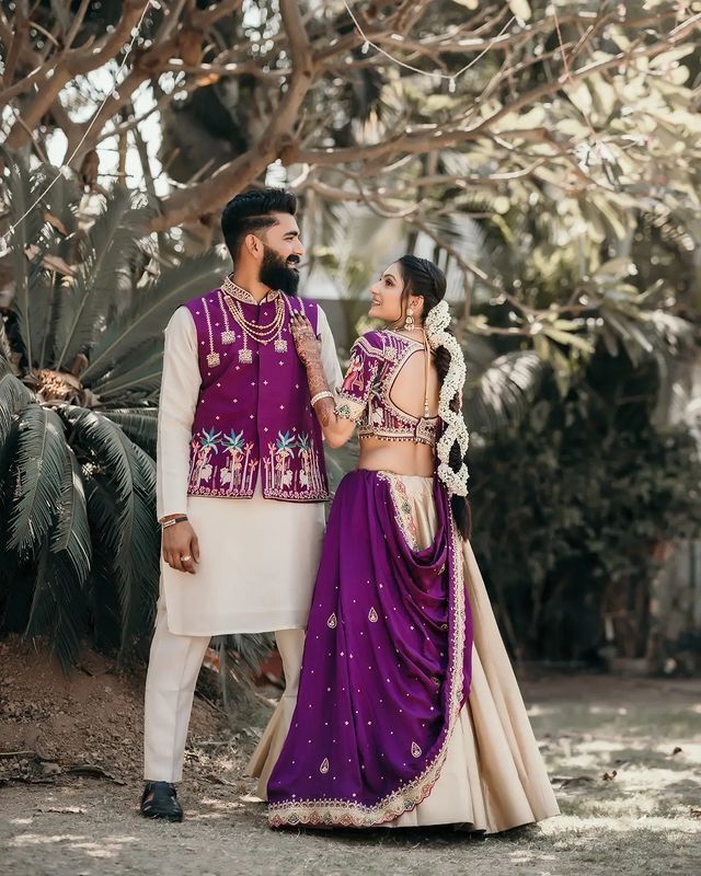 a man and woman standing next to each other in front of some trees with their arms around each other