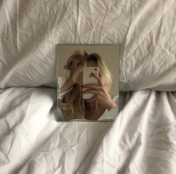 a woman is taking a selfie with her cell phone in the mirror on a bed