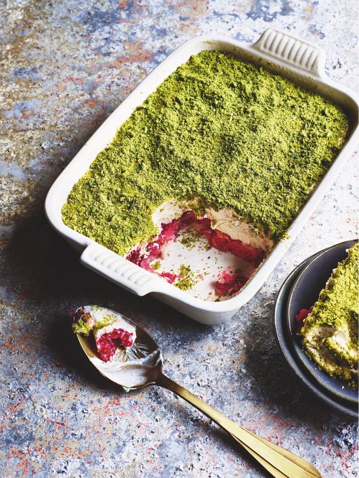 a casserole dish filled with pesto and white sauce next to two spoons