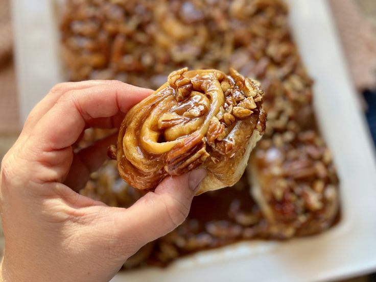 a person is holding some kind of food in front of a plate full of baked goods