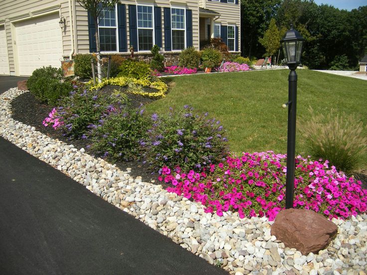 a house with flowers in front of it and a lamp post next to the driveway