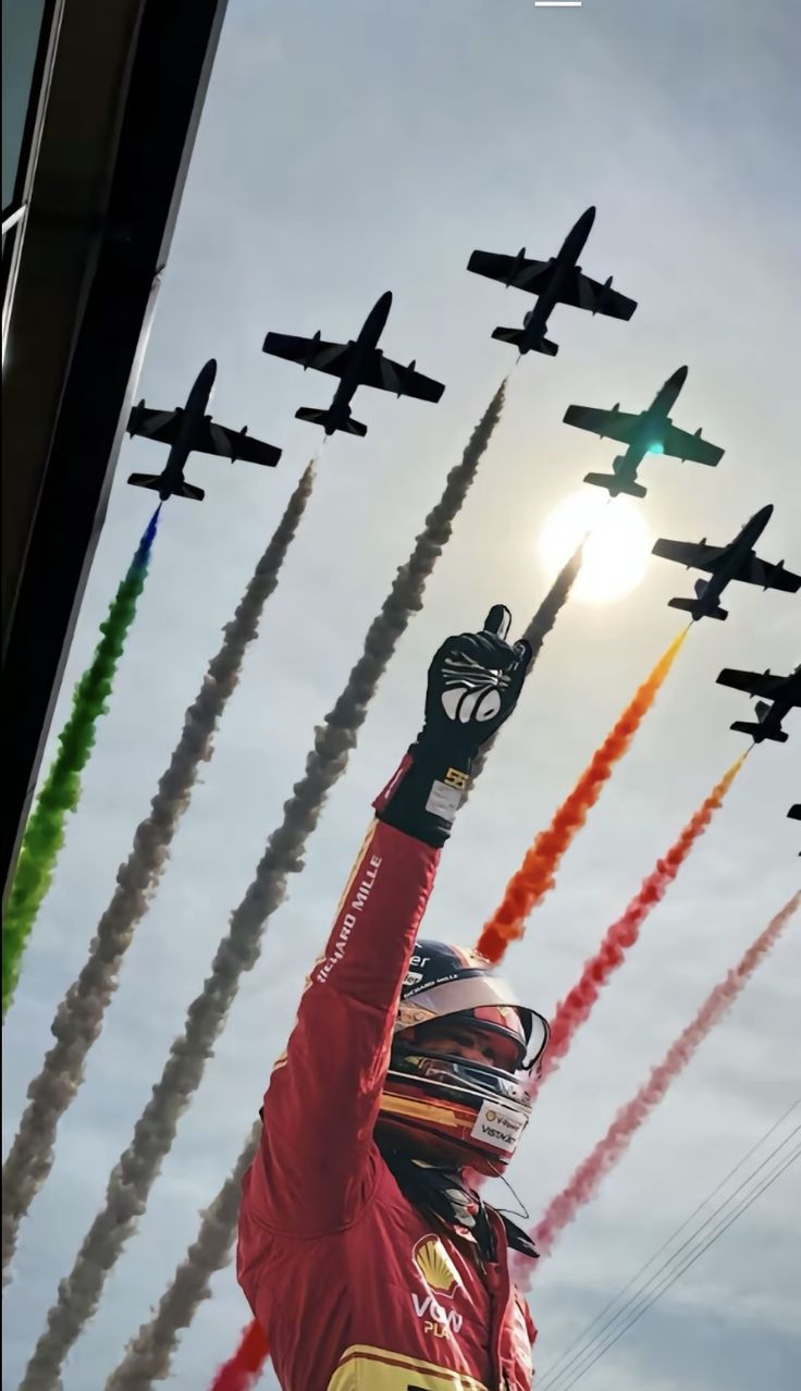 a man holding his arm up in the air with jets flying behind him and onlookers watching