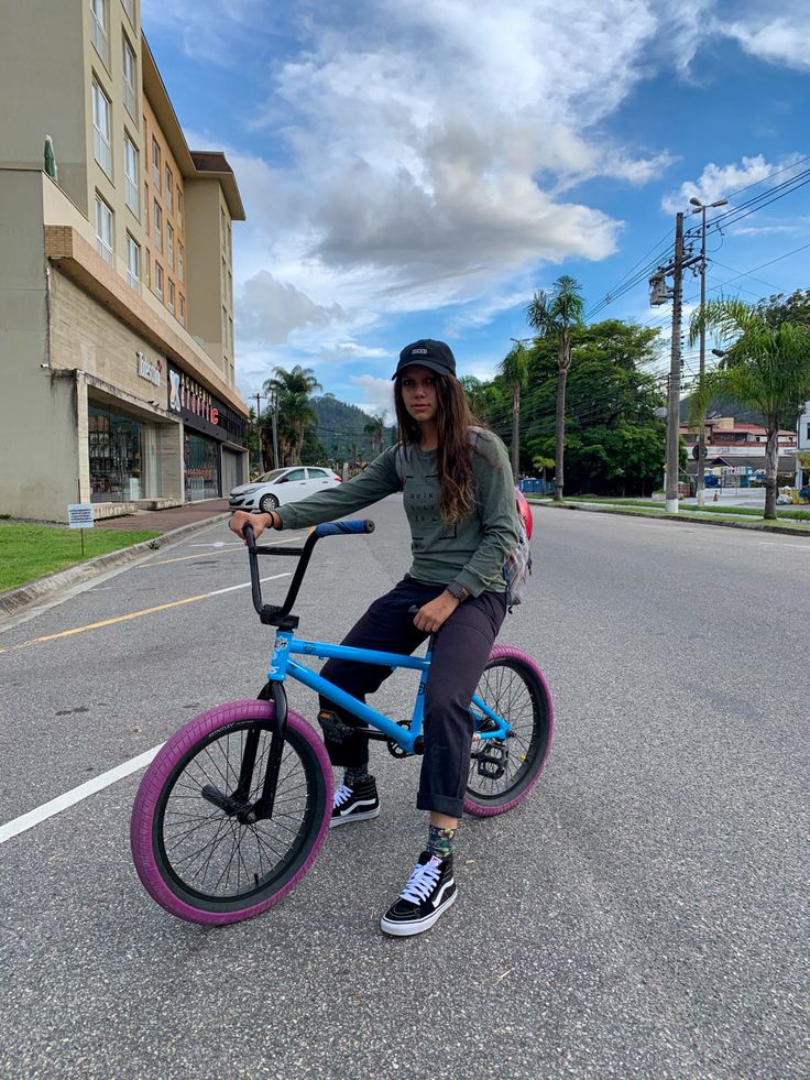 a woman riding a blue bike down a street next to a tall building with purple rims