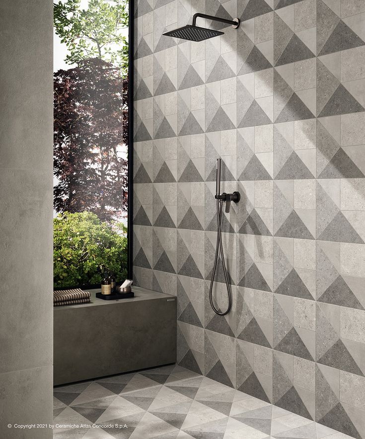 a bathroom with grey and white geometric tiles on the wall, shower head, and hand held shower faucet