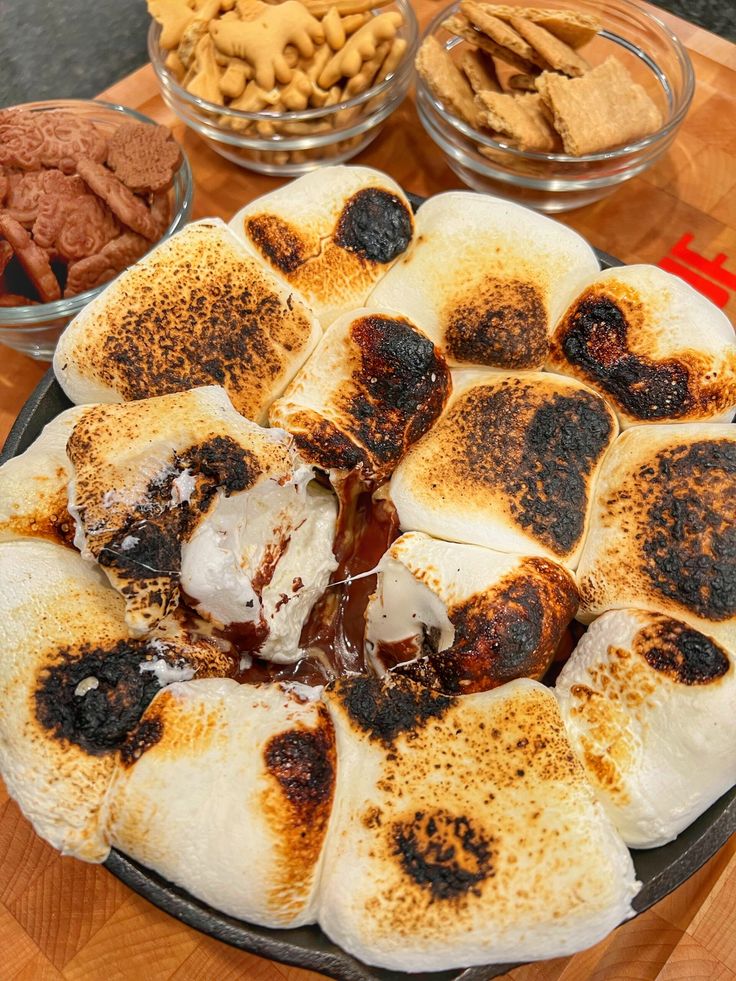 a pizza sitting on top of a wooden table next to bowls of nuts and crackers