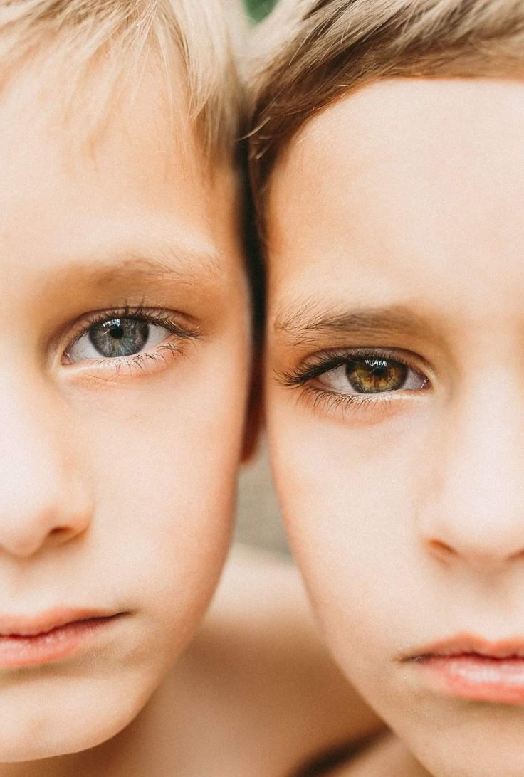 two young boys with brown eyes are looking at the camera while one boy is holding his head up