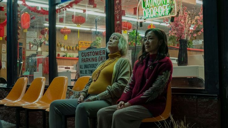 two women sitting on yellow chairs in front of a store window with chinese lanterns hanging from the ceiling