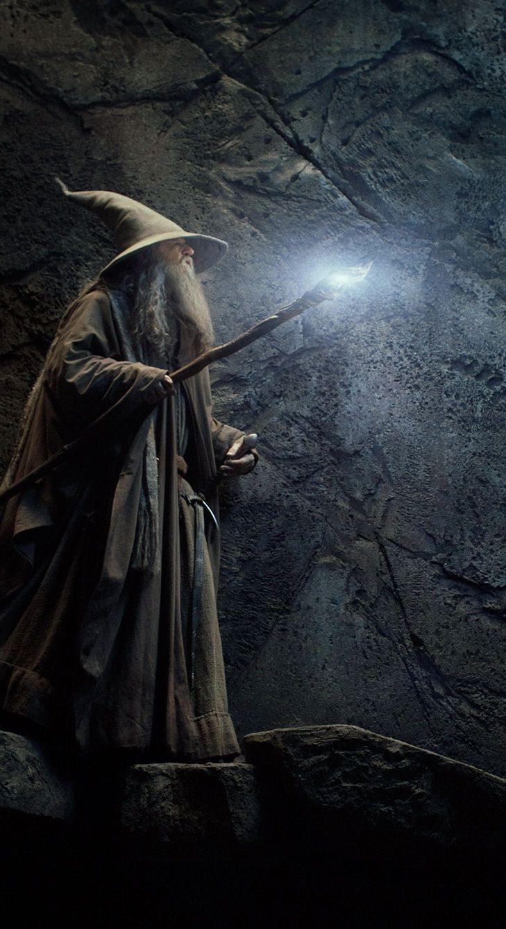 a wizard holding a light in his hand and standing on a rock formation with dark background