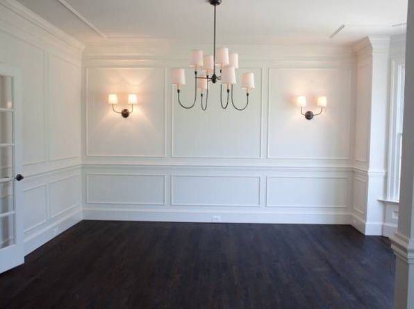 an empty room with white walls and wood floors, chandelier hanging from the ceiling