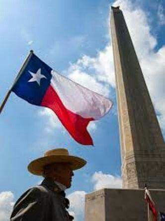 a man wearing a hat and holding a texas flag in front of a tall obelisk