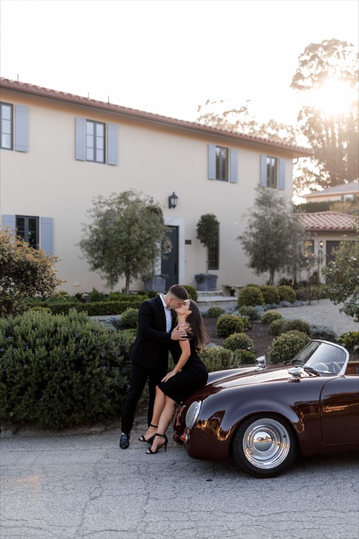 a man and woman kissing in front of an old car